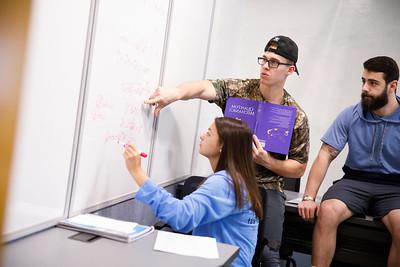 toll fellows, two boys and a girl student working together on a physics problem at a whiteboard